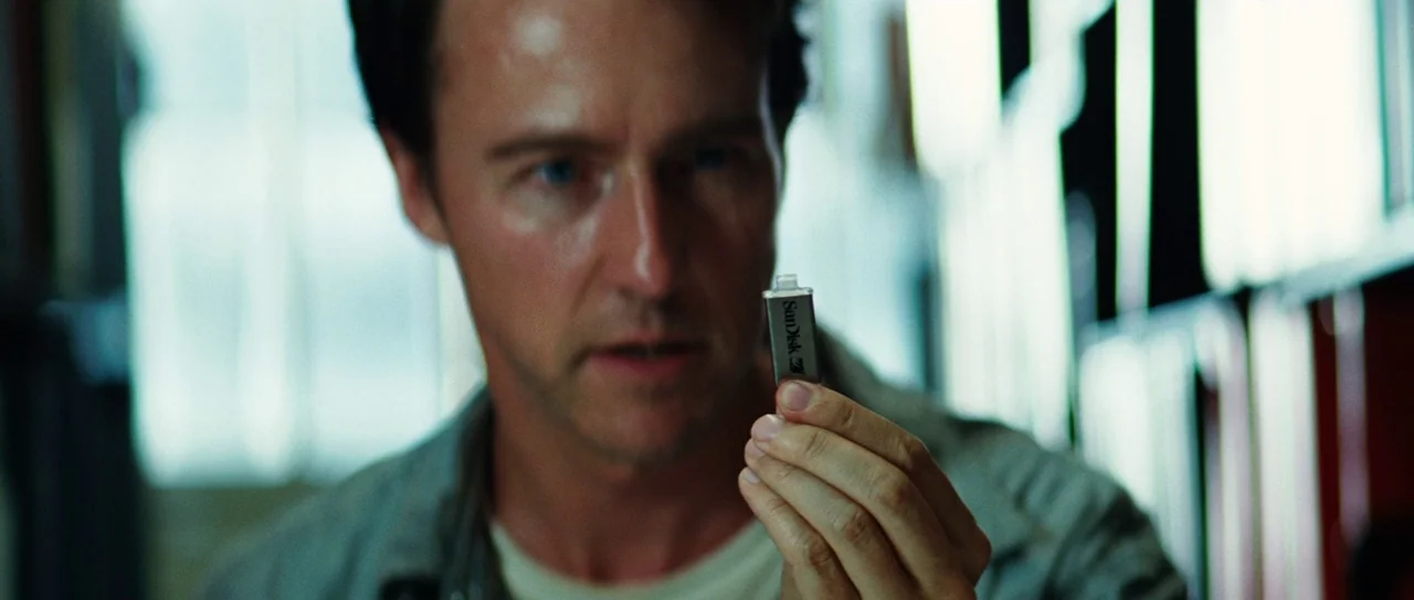 The Incredible Hulk (2008) movie still: closeup — An interior space contains a man looking closely at a small object. He holds a silver USB drive in…