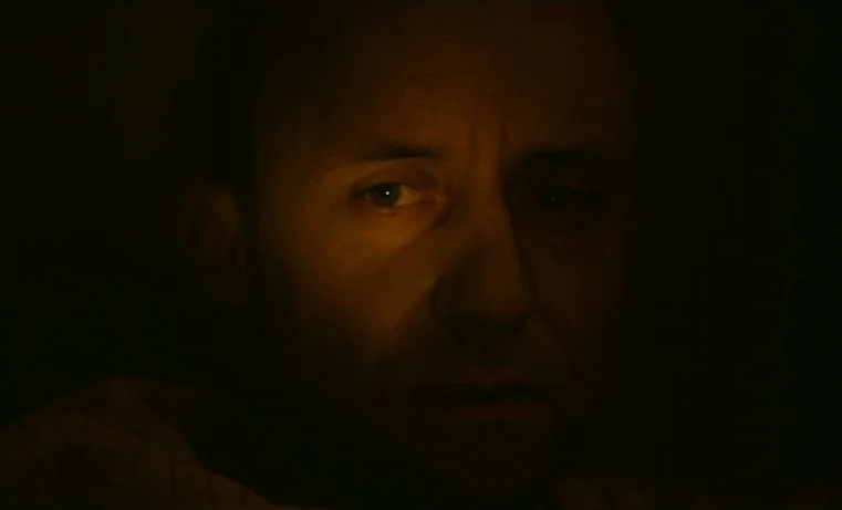 Golem (1980) movie still: closeup — A man's face emerges from complete darkness in a room at night. He is illuminated by a single warm light source…