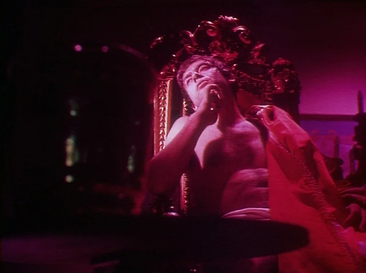 Hermitage (1968) movie still: medium — A man sits on a ornate, high-backed wooden chair in a dark room. The scene is bathed in intense magenta light…
