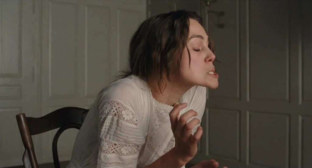 A Dangerous Method movie still: medium — A spartan room with plain grey paneled walls and a wooden chair. A young woman in a white lace blouse sits…