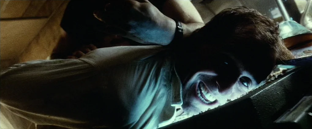 Minority Report movie still: closeup — A dimly lit interior space with dark textures and deep shadows surrounding the subject. A man in a white…