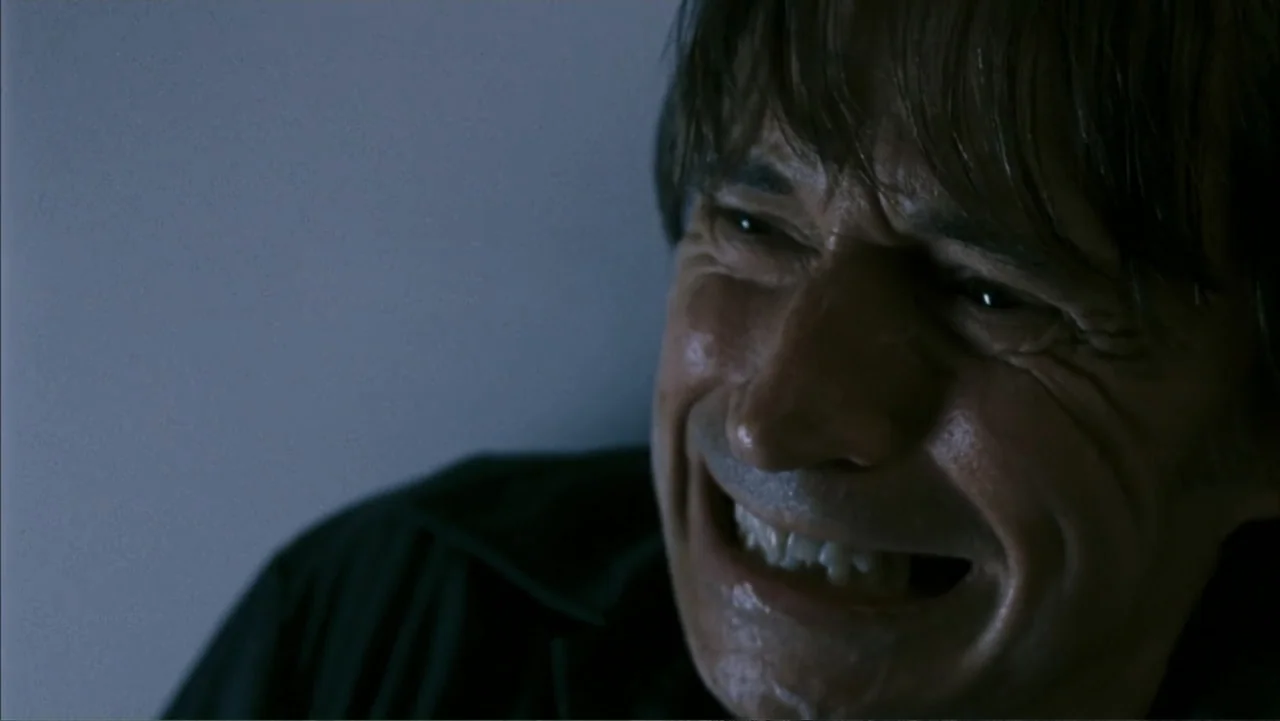 28 Weeks Later (2007) movie still: closeup — A dark indoor space with minimal ambient light and blue-tinted shadows. A man in his fifties looks…