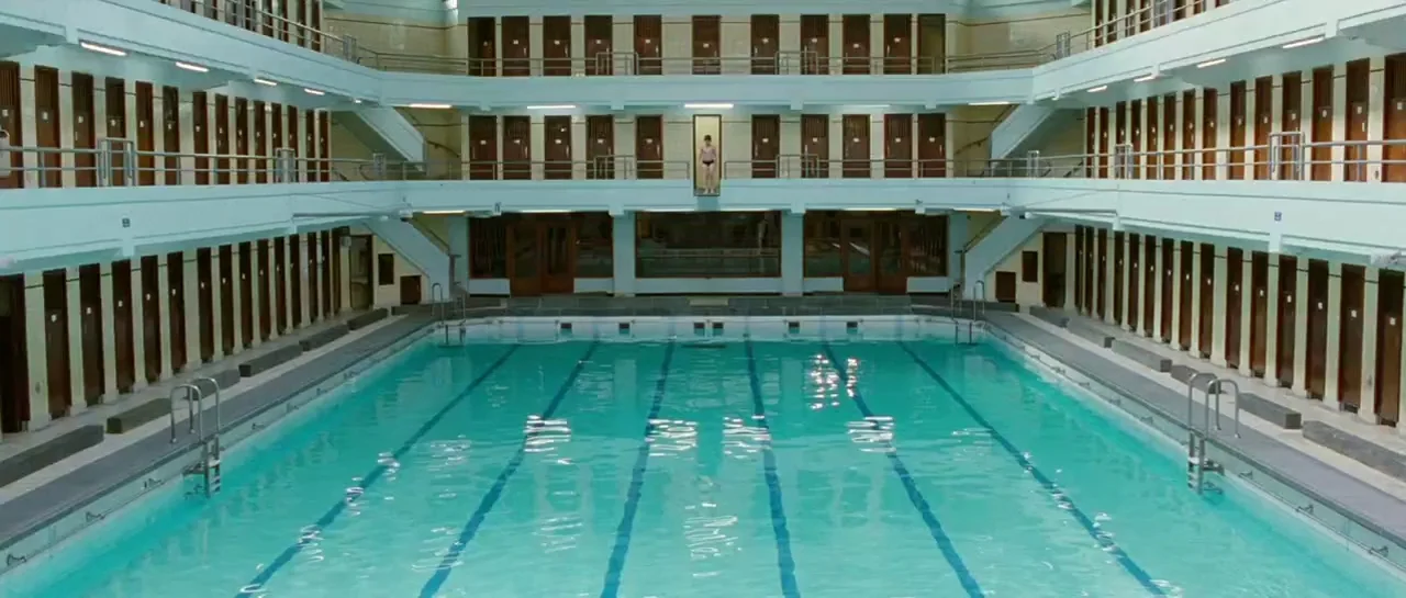 Mr. Nobody (2009) movie still: wide — A symmetrical indoor swimming pool features multiple levels of private changing cabins. A small child stands…