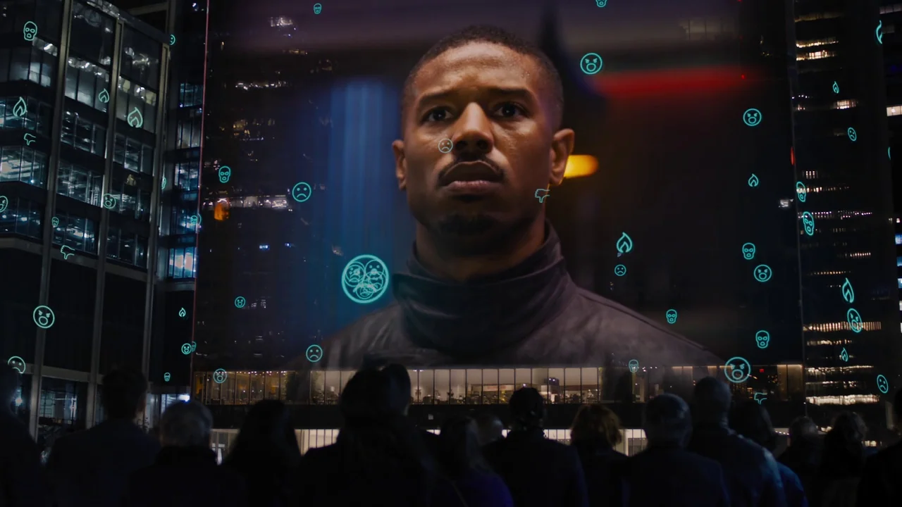 Fahrenheit 451 (2018) (2018) movie still: wide — A nighttime urban square features a massive digital screen displaying a man's face. A crowd of…