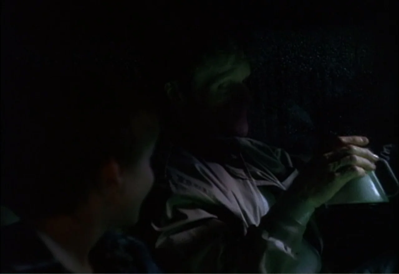 Ambushed (1998) movie still: medium — Two individuals occupy the dark front seats of a vehicle at night. A person in the passenger seat holds a…