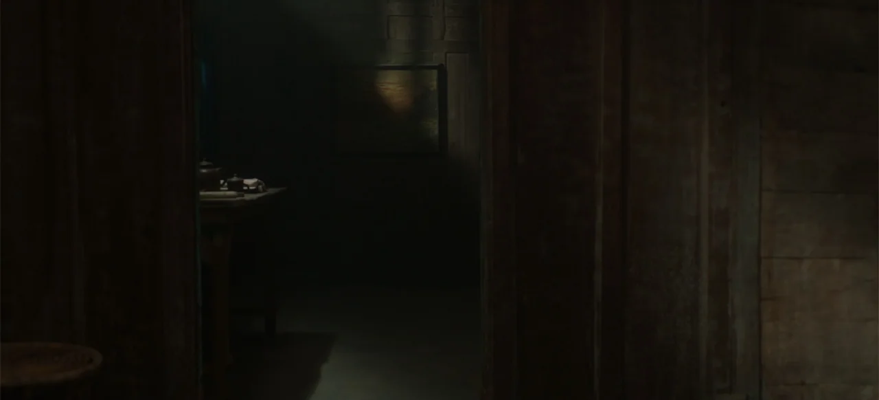 A Thousand Days (2023) movie still: establishing — A dark wooden room with a single shaft of light hitting a framed painting. A small side table…
