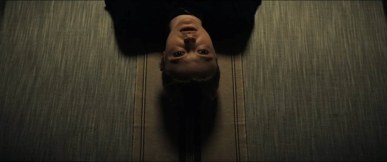 Vicious (2025) movie still: closeup — A person lies on a textured, striped surface oriented vertically in the frame. The subject rests on a surface…