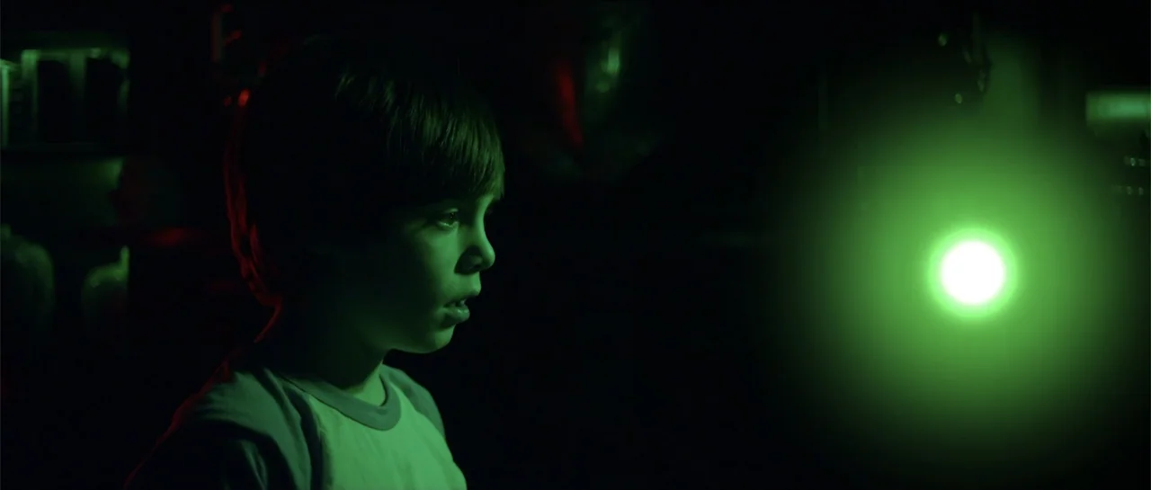 Halloween III: Season of the Witch (1982) movie still: closeup — A dark room is illuminated by a single glowing green light source. A young boy…