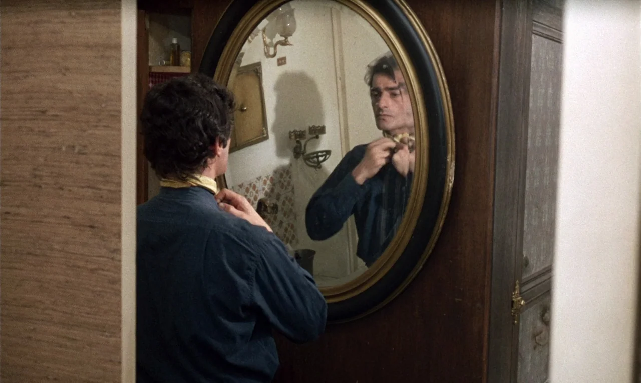 The Bride Wore Black (1968) movie still: medium — A man stands in front of an oval mirror mounted on a wooden frame. He carefully adjusts a scarf…