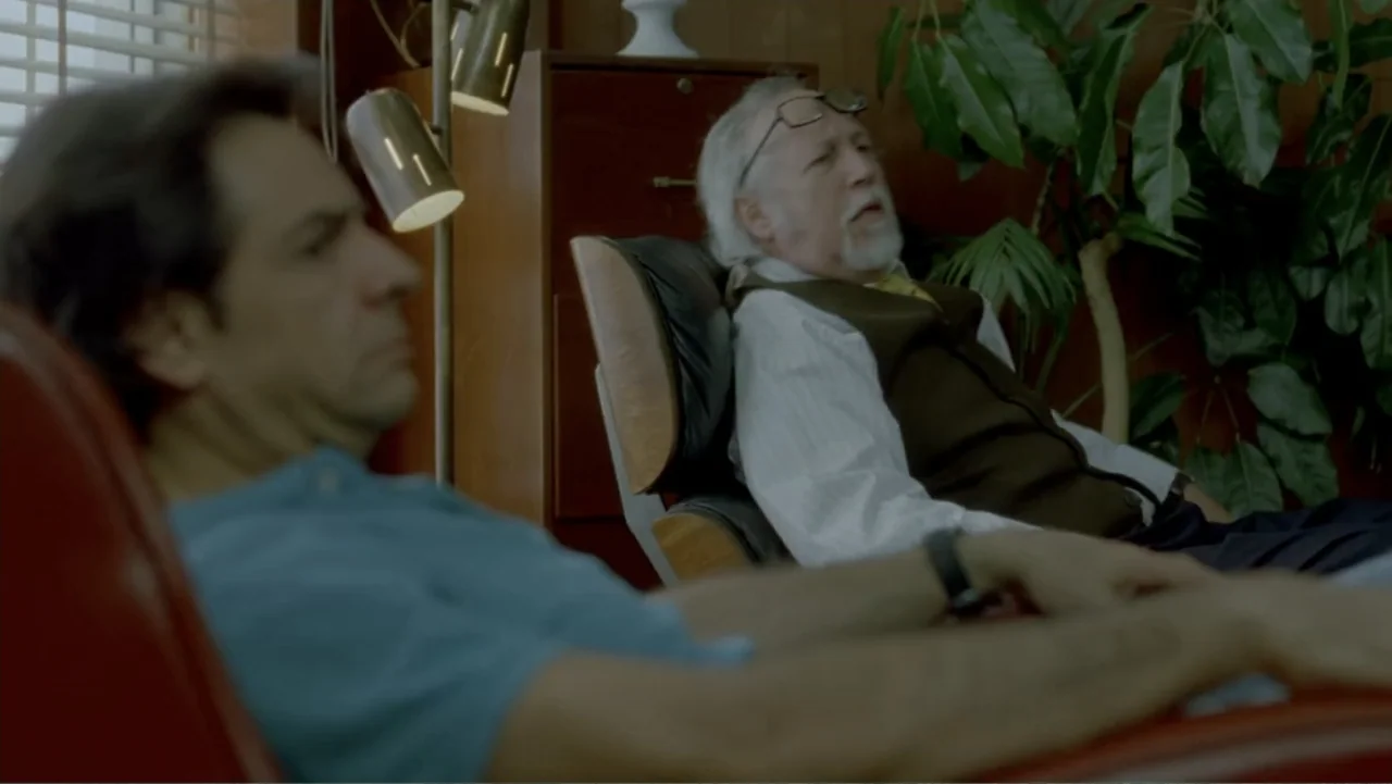 George Lopez: It's Not Me, It's You (2012) movie still: medium — An office interior features wood paneling, a leafy plant, and a metal cabinet. An…