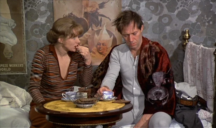 The Serpent’s Egg (1977) movie still: medium — Two people sit on a bed beside a small wooden table covered with food. Behind them is a wall…