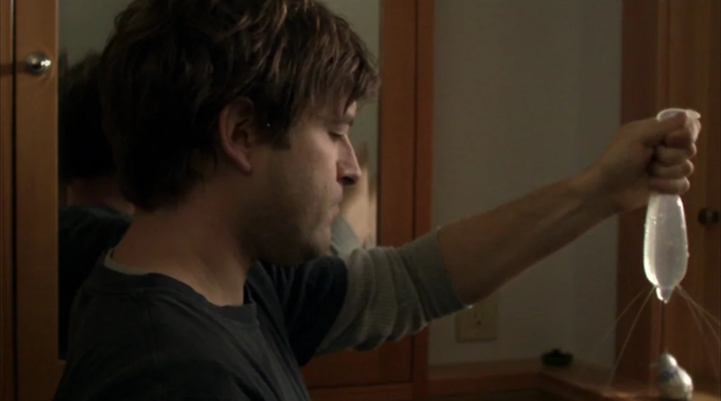 Your Sister’s Sister (2011) movie still: medium — A man stands in a small bathroom with wood-toned cabinetry and vanity mirrors. He holds a…