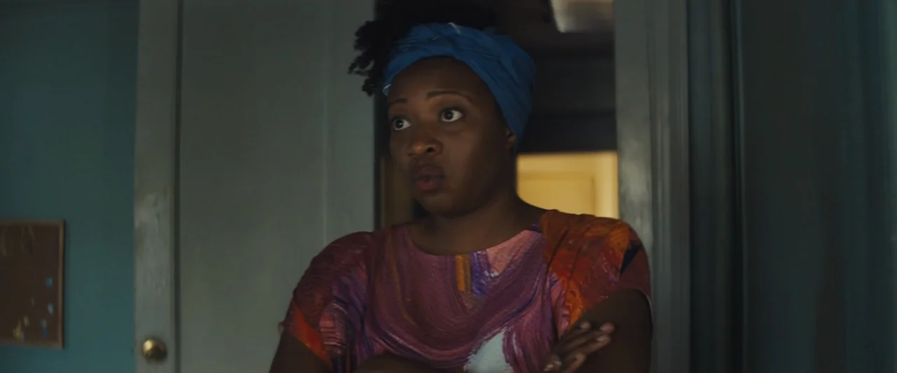 The Sun Is Also a Star (2019) movie still: medium — A woman stands in a doorway between a blue room and a brighter space. She has her arms crossed…