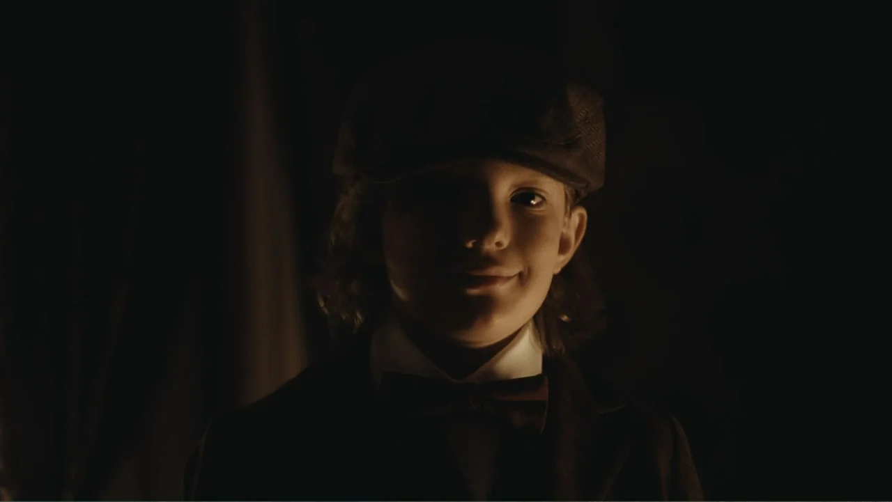 Demon in the White House (2021) movie still: closeup — A dark, dimly lit interior space with the subject centered in the frame. A young boy in 1920s…