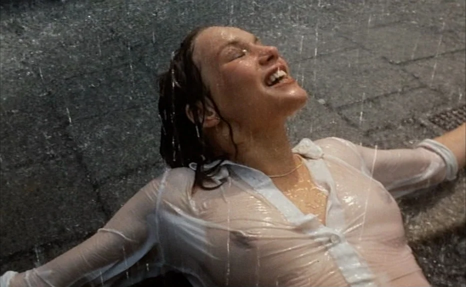 Turkish Delight (1973) movie still: medium — A woman lies on wet asphalt pavement during a nighttime rain shower in city. She stares upward with her…