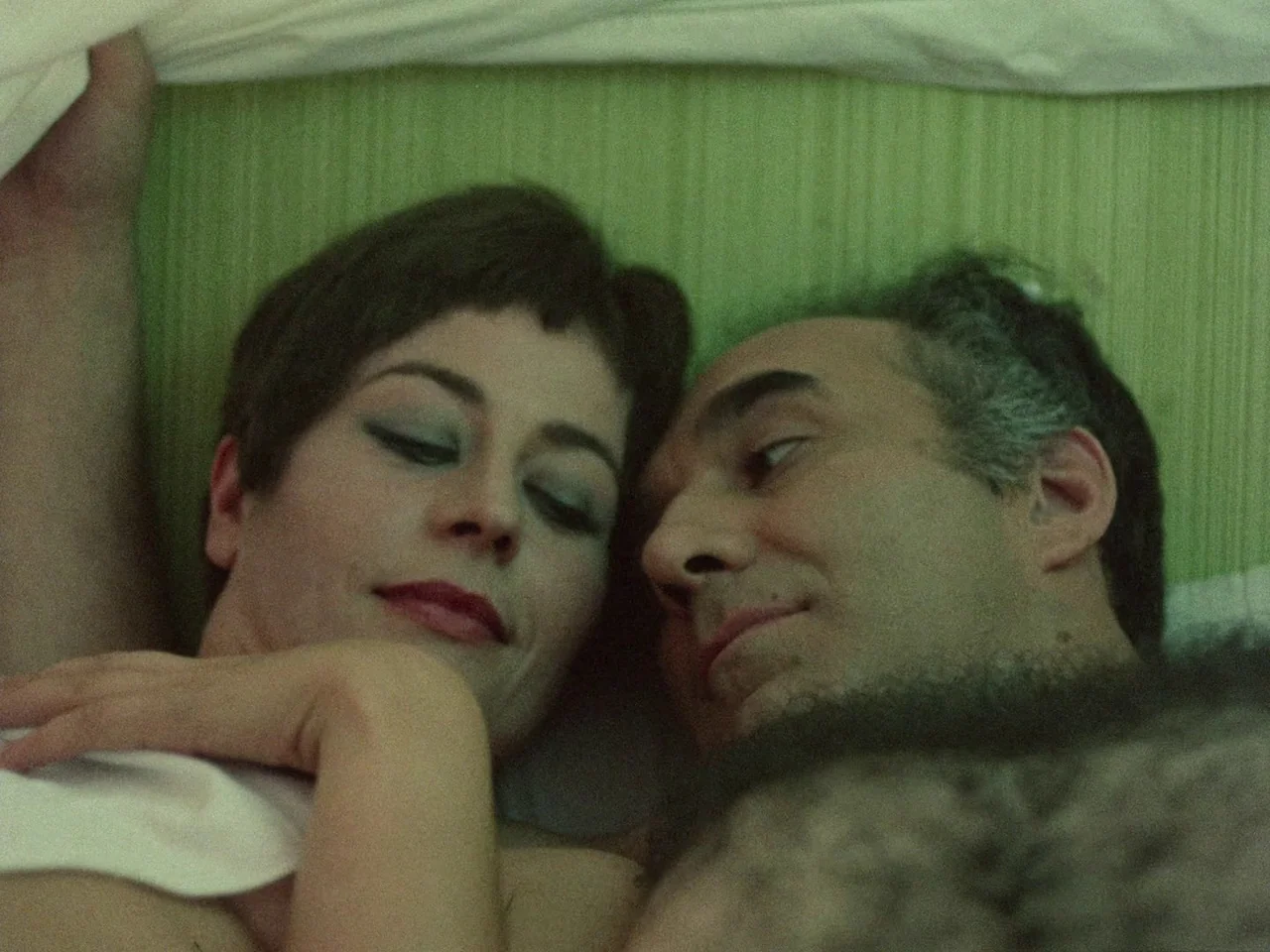 Dillinger is Dead (1969) movie still: closeup — Two individuals lie close together on a light green mattress under white covers. The scene shows the…