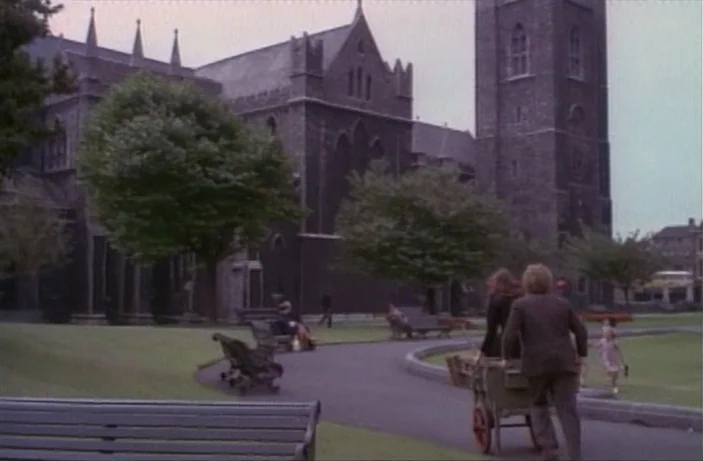Quackser Fortune Has a Cousin in the Bronx (1970) movie still: wide — A dark stone gothic cathedral looms over a public park with manicured grass…