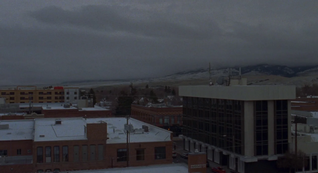 Certain Women (2016) movie still: establishing — A small town downtown area with brick buildings is covered in light snow. Mountain ranges are…