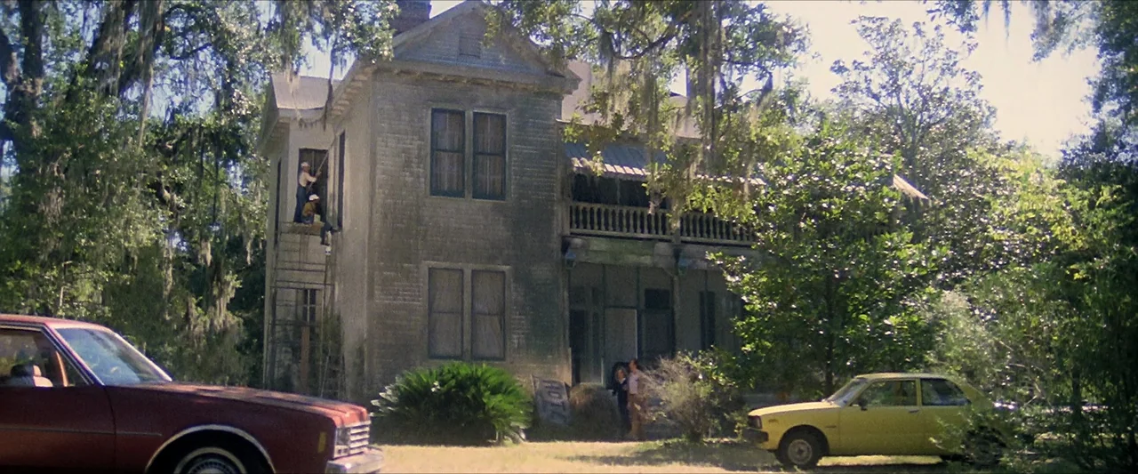 The Beyond (1981) movie still: wide — An aging two-story Southern house is surrounded by large trees draped in Spanish moss. Two workers stand on…