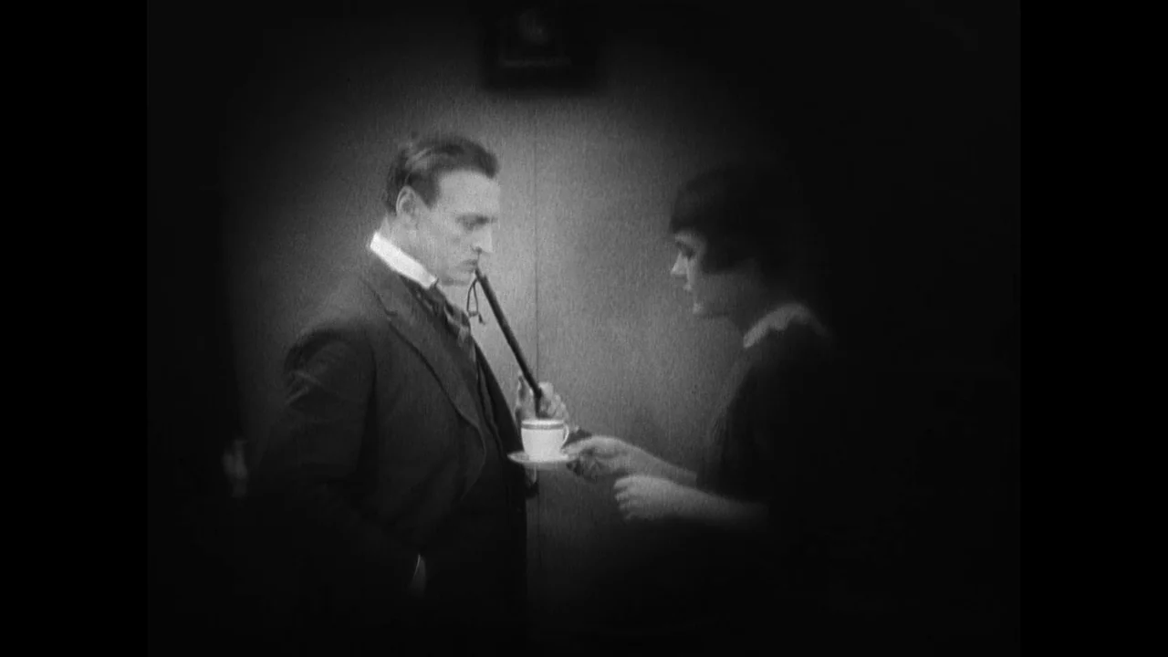 Master of the House (1925) movie still: medium — A dark indoor space features two people standing facing each other in vignette framing. A man holds…