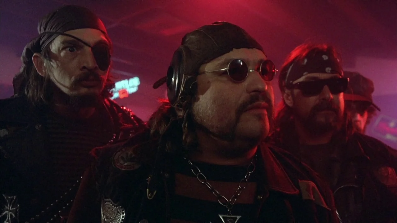 Pee-Wee’s Big Adventure (1985) movie still: medium — Three men dressed in biker attire stand close together in a dimly lit space. They remain…