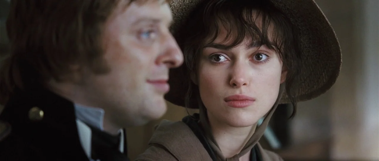 Pride & Prejudice (2005) movie still: closeup — A dimly lit interior space with soft textures visible on clothing and accessories. Two individuals…