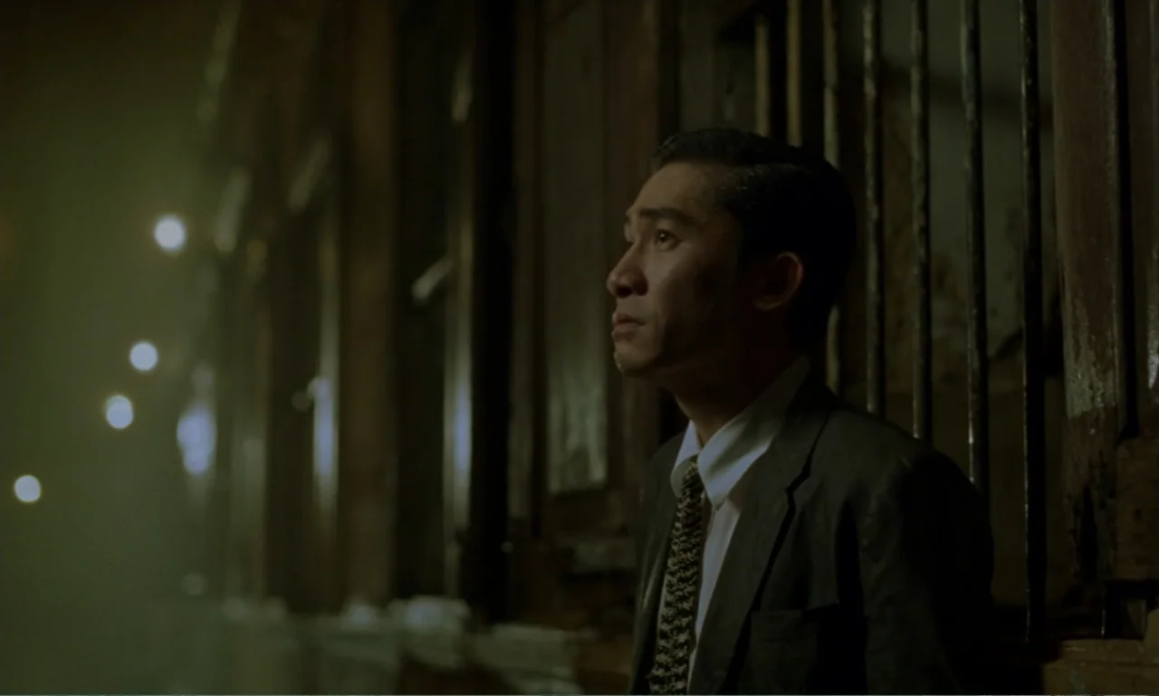 In the Mood for Love (2000) movie still: medium — A dark alleyway features brick walls and vertical metal bars set into the side. A man in a…