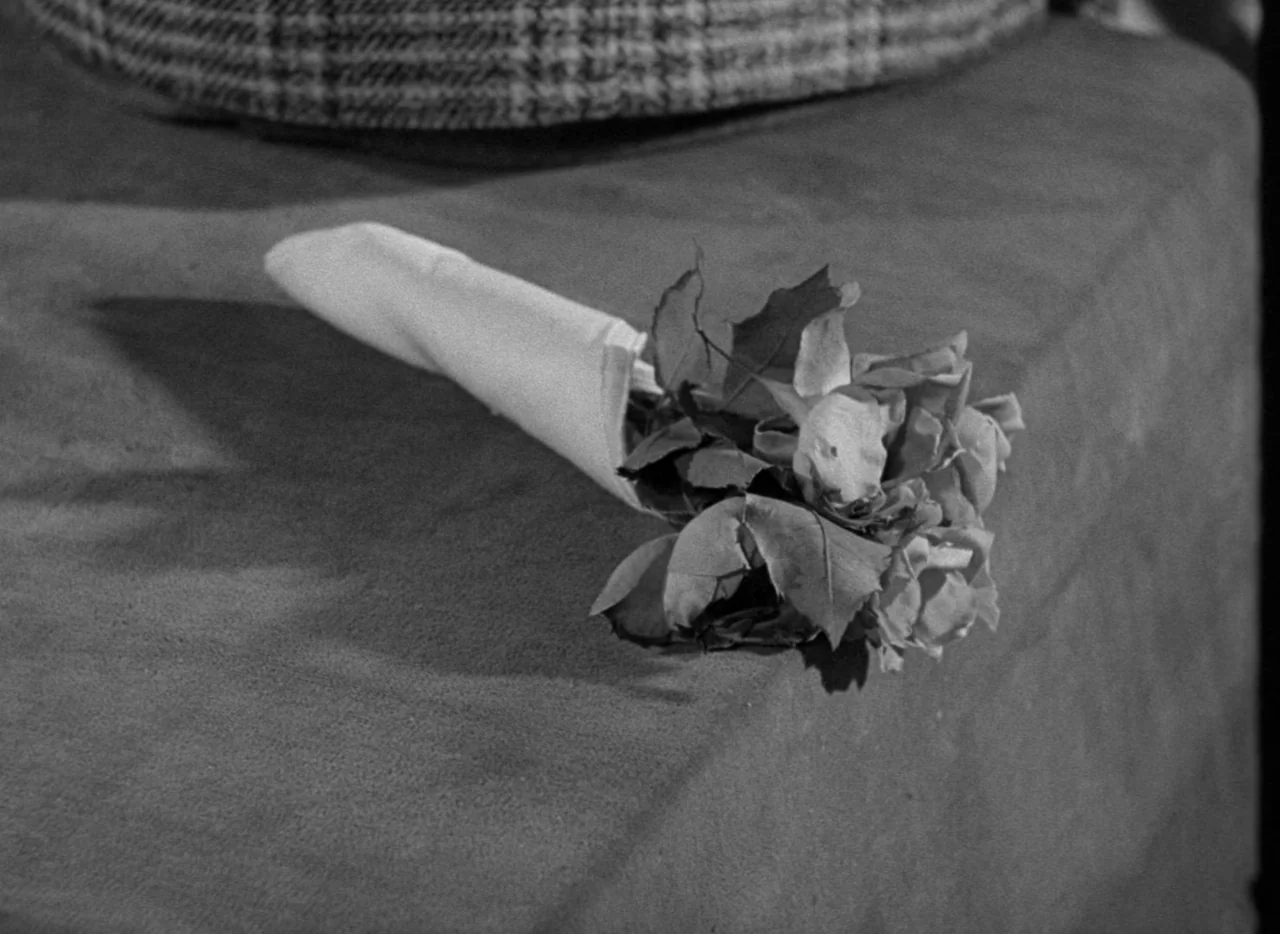 The Uninvited (1944) movie still: closeup — A small bouquet of roses is wrapped in paper and sits on a fabric surface. A patterned textile is…