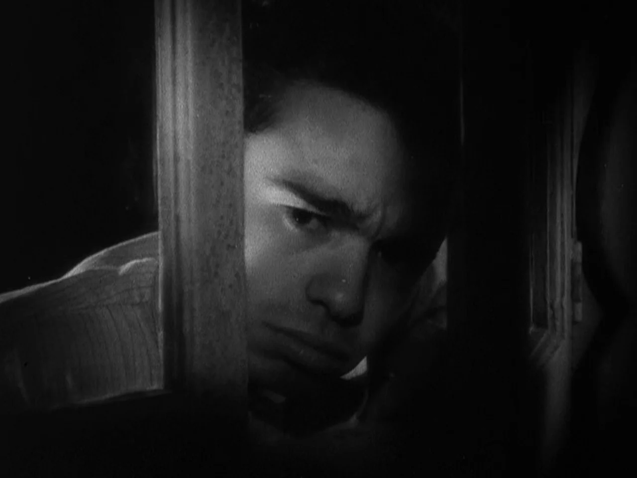 Freaks (1932) movie still: closeup — A dark, cramped space frames a man looking through a narrow vertical opening. The man peers cautiously through…
