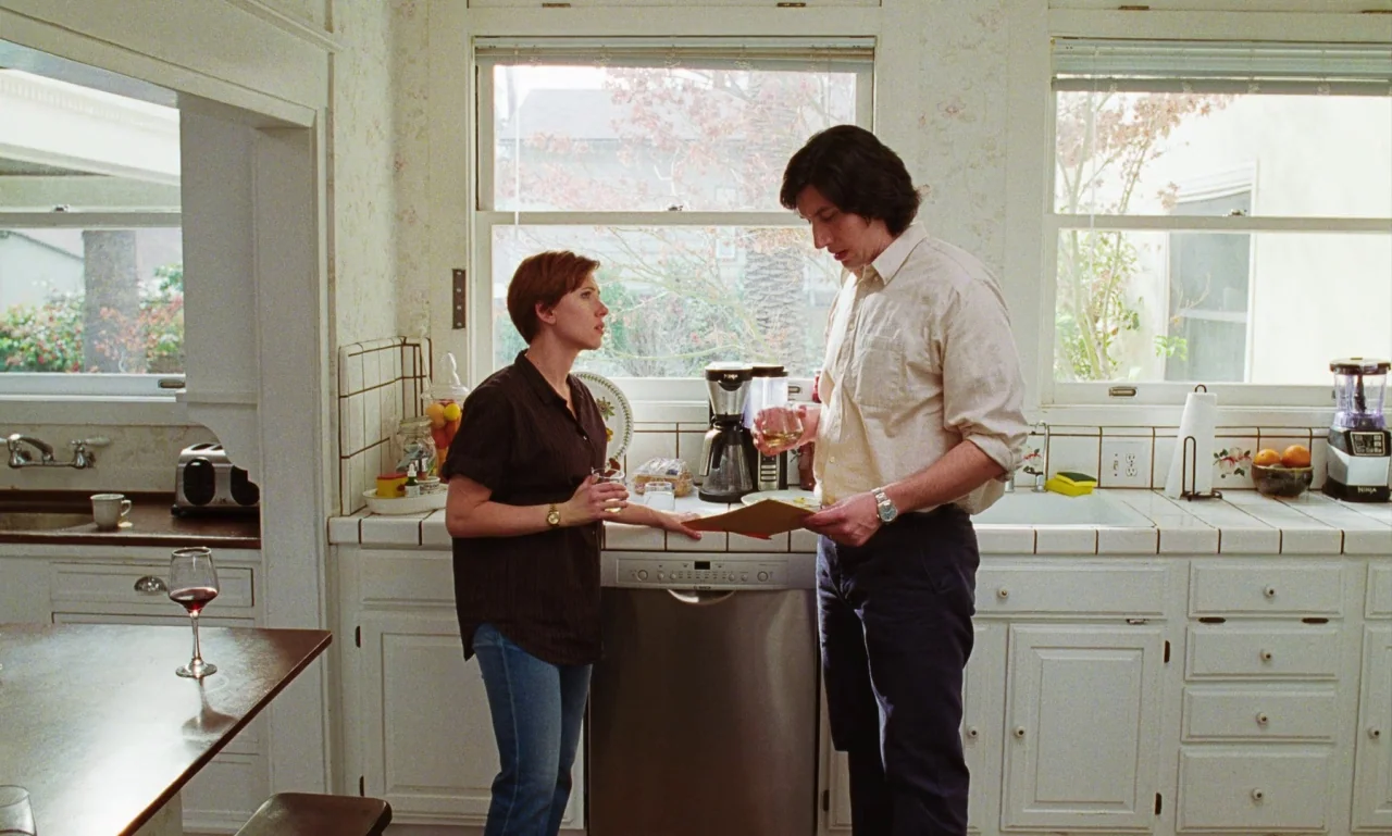 Marriage Story movie still: medium — A residential kitchen features white cabinets, tiled countertops, and large windows looking outside. A woman in…