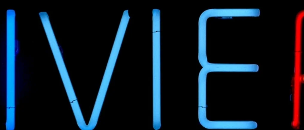 Pierrot Le Fou (Crazy Pete) (1965) movie still: closeup — A close-up view of a neon sign against an dark background at night. The blue glowing tubes…