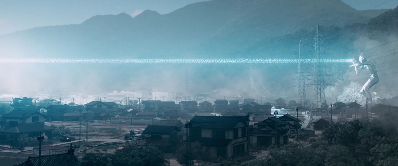 Shin Ultraman (2022) movie still: wide — A rural Japanese town sits in a hazy valley surrounded by green forested mountains. A giant silver humanoid…