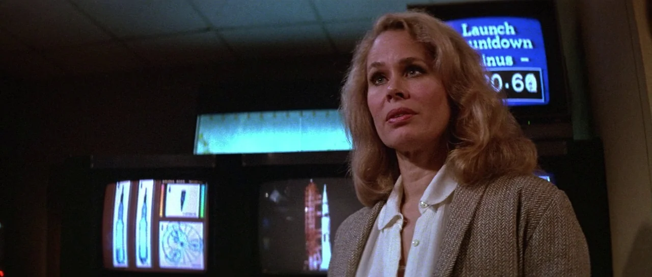 Invaders From Mars (1986) movie still: medium — A dimly lit control room filled with flickering monitors displaying data and space imagery. A blonde…