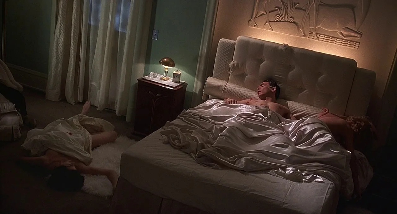 Chicago (2002) movie still: wide — A dimly lit 1940s hotel suite features green walls and a large, tufted bed. A man and two women are sprawled…
