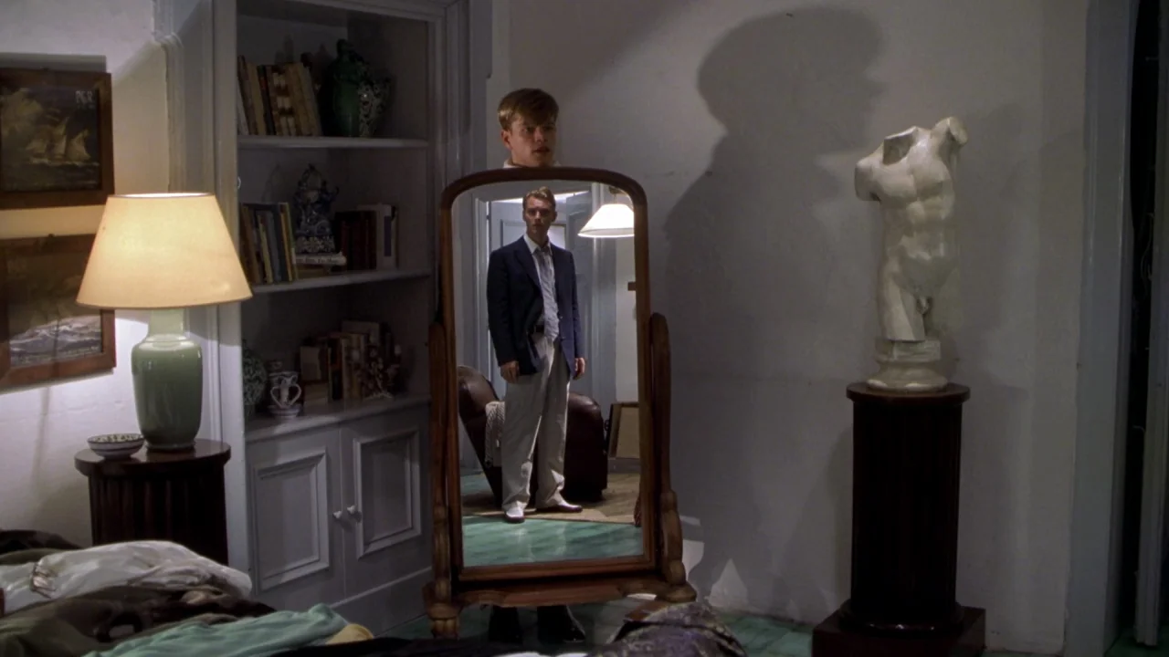 The Talented Mr. Ripley (1999) movie still: medium — A room contains a bookshelf, a table lamp, and a marble torso statue. A man stands before a…