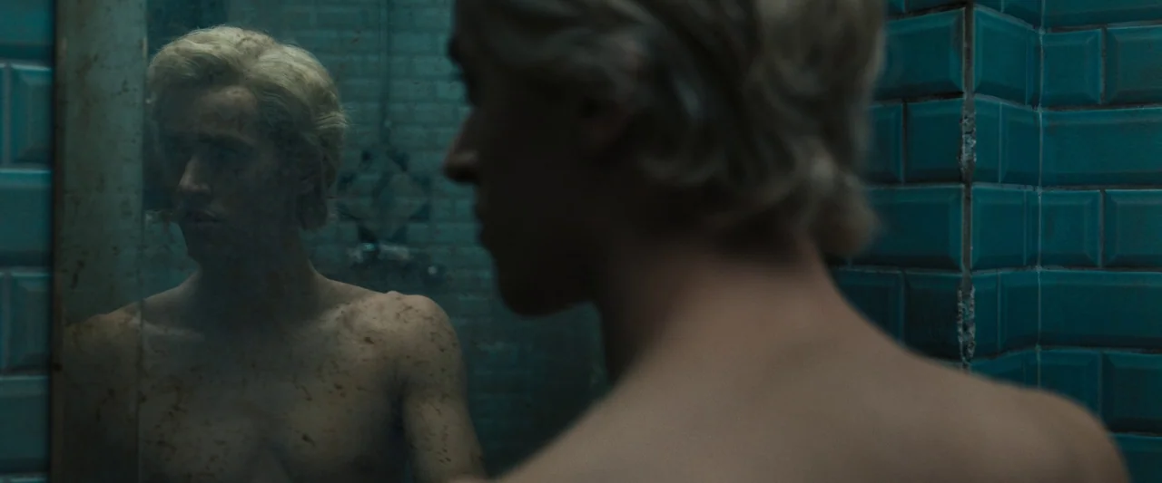 The Hunger Games: The Ballad of Songbirds & Snakes (2023) movie still: medium — A dimly lit room features teal subway tiles on the walls. A…