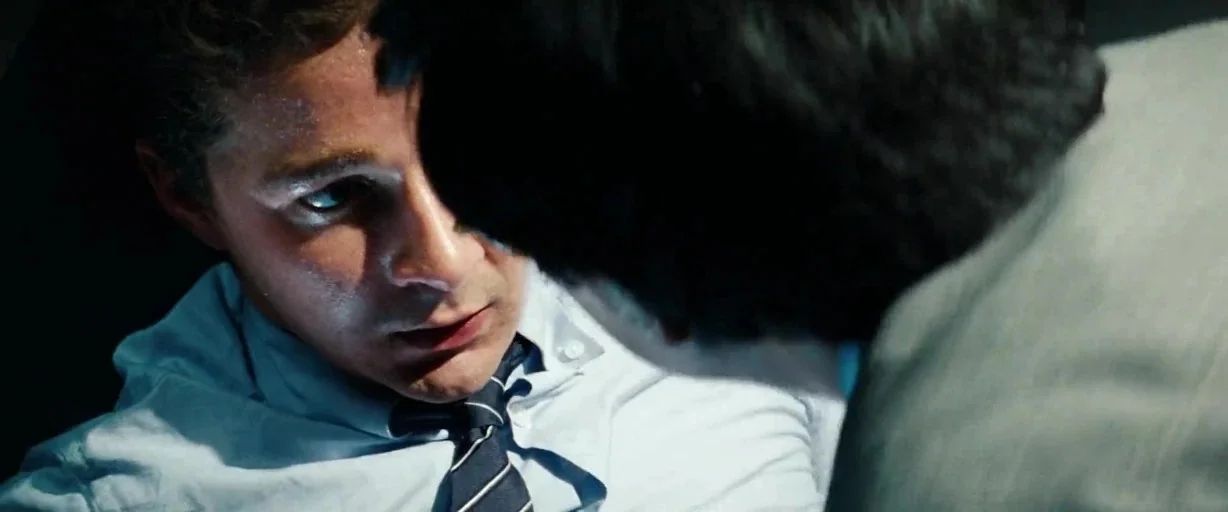 Transformers: Dark of the Moon (2011) movie still: closeup — A man sits inside a dark vehicle while illuminated by a sharp side light. He looks…
