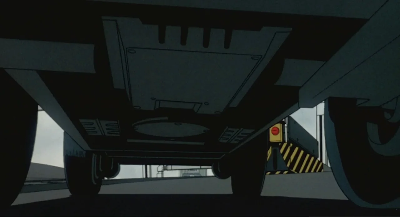 Ghost in the Shell (1995) movie still: wide — A low-angle view from beneath a vehicle on an asphalt road during the day. A metal barrier with yellow…