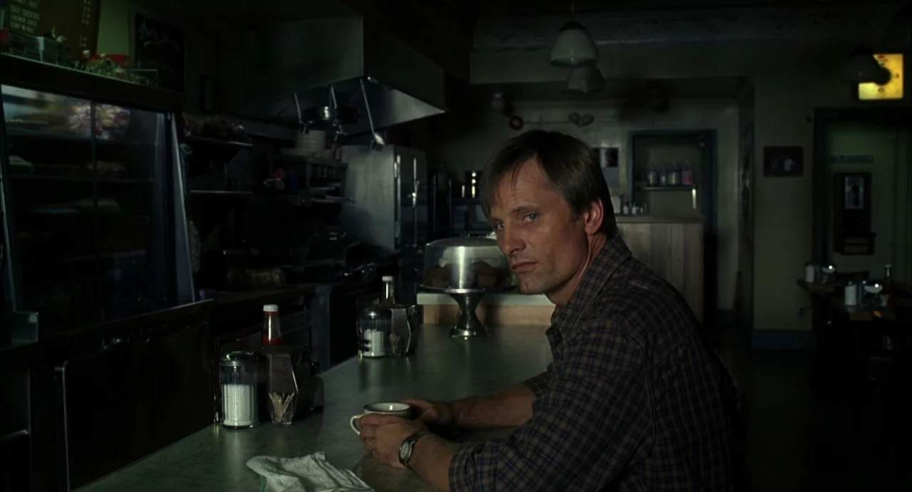 A History of Violence (2005) movie still: medium — A dimly lit diner with a long counter and a stainless steel prep area. A man sits at the counter…