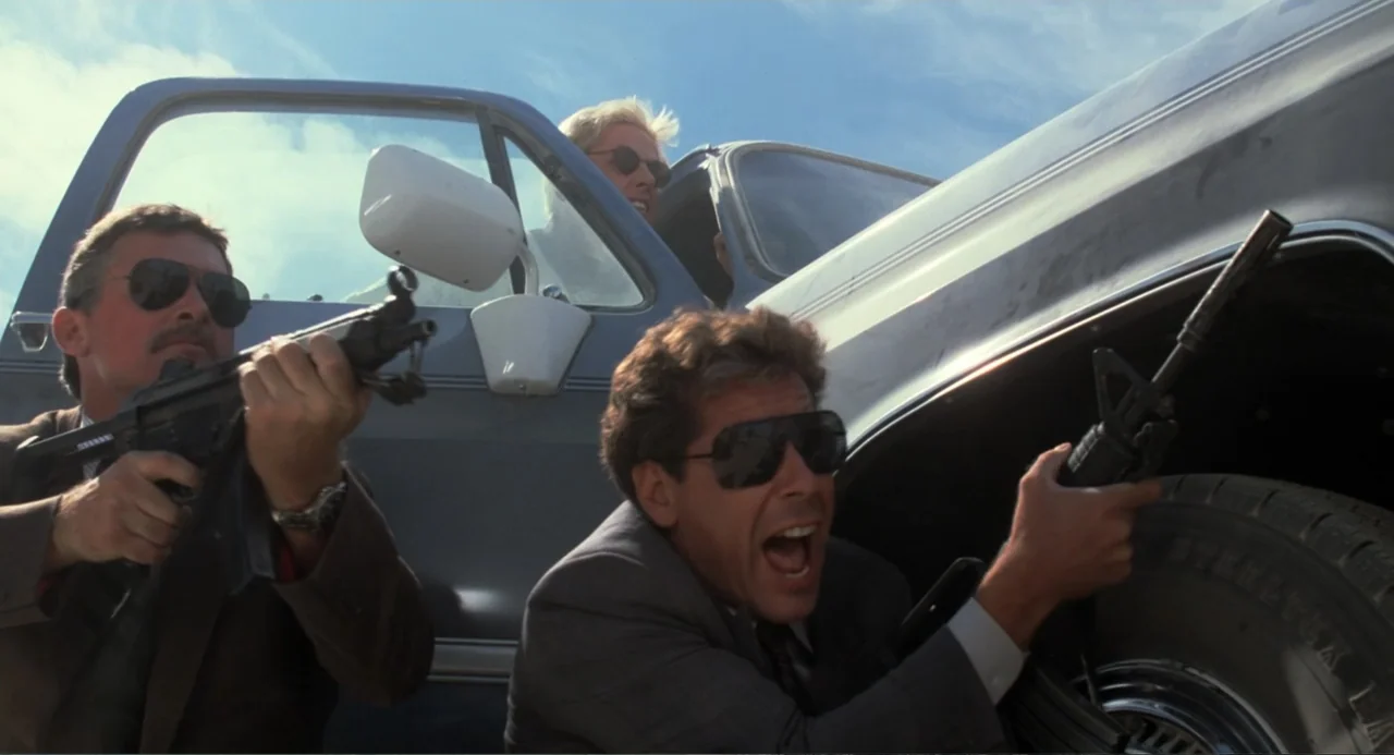 Lethal Weapon (1987) movie still: medium — Three armed men in suits hide behind the side of a blue pickup truck. They brandish rifles and handguns…