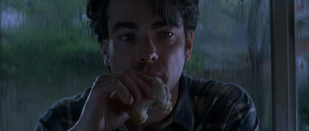 The Underneath (1995) movie still: closeup — A man sits in front of a rain-streaked window. He is eating a piece of bread while looking forward.