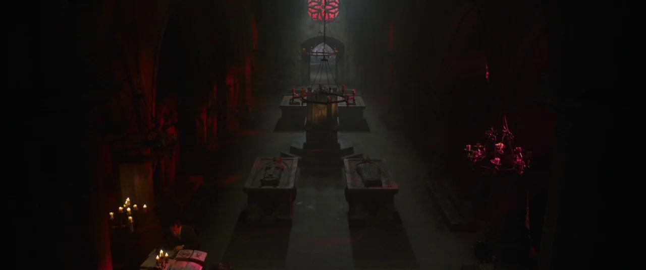 The Nun (2018) movie still: wide — A stone crypt features ancient sarcophagi, arched ceilings, and a stained glass rose window. A single man sits at…