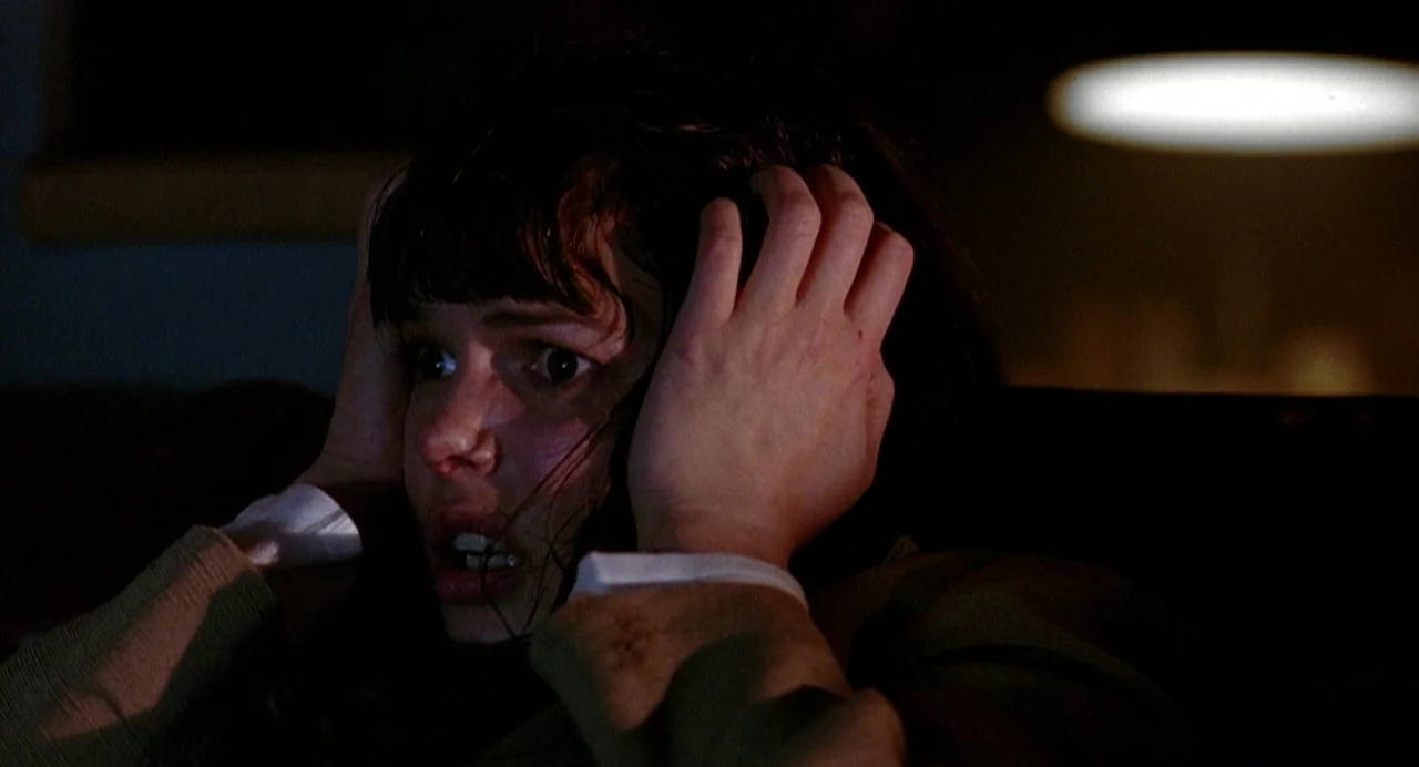 Office Killer (1997) movie still: closeup — A dimly lit indoor space with dark, indistinct surroundings behind the subject. A young woman with dark…