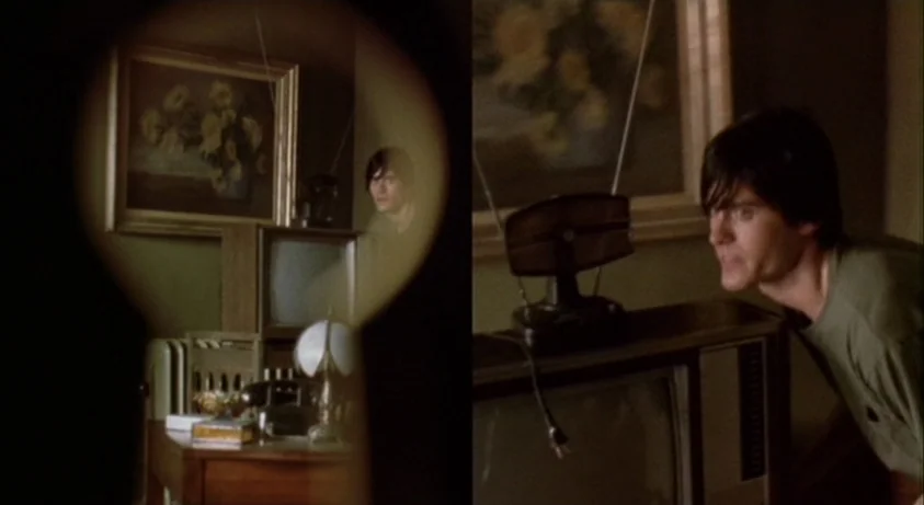 Requiem For A Dream (2000) movie still: medium — A dimly lit apartment room contains a vintage television and an framed oil painting. A young man…