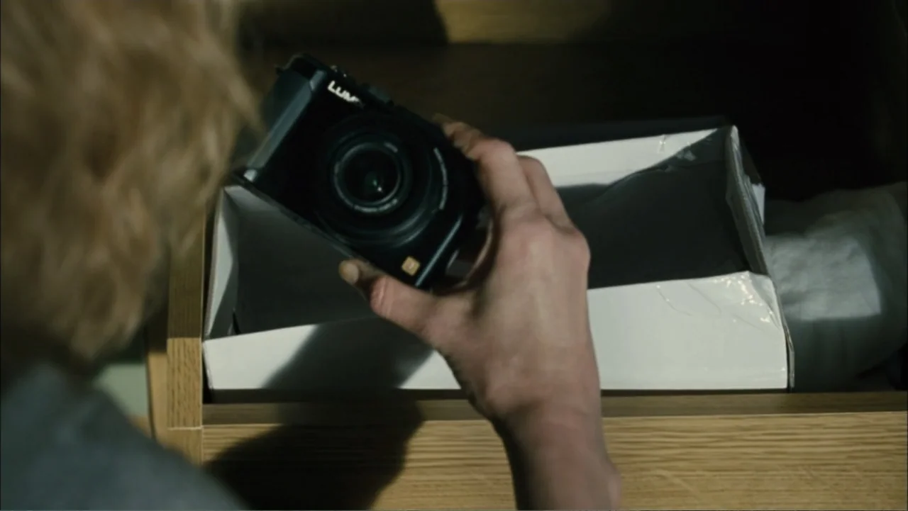 Before I Go to Sleep (2014) movie still: closeup — A wooden dresser drawer contains a white cardboard box holding a small black camera. A person…