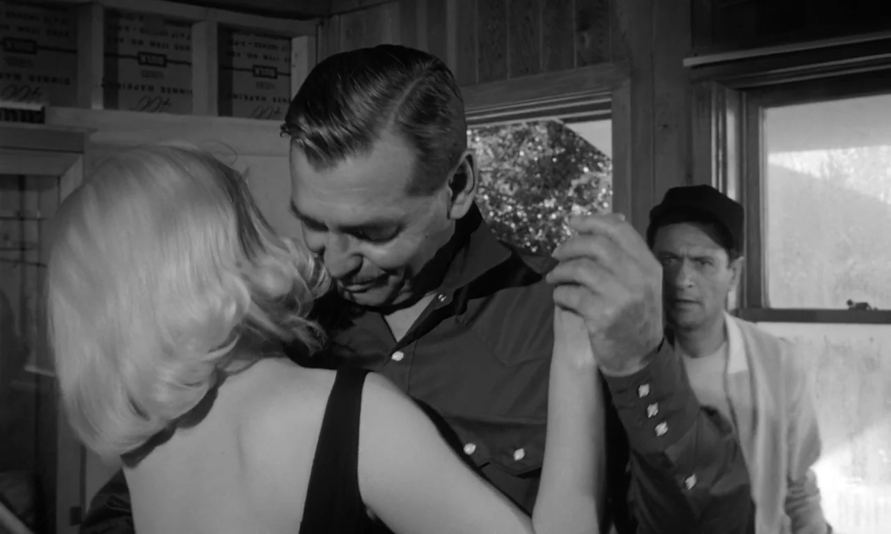 The Misfits (1961) movie still: medium — A cluttered interior space features wooden wall panels and stacked inventory boxes. A couple dances…