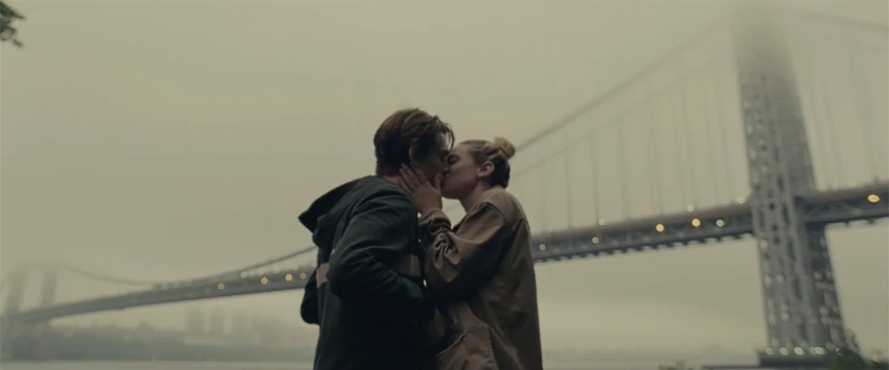 Chemical Hearts (2020) movie still: medium — An outdoor riverside promenade features a large suspension bridge visible in thick gray fog. A young…