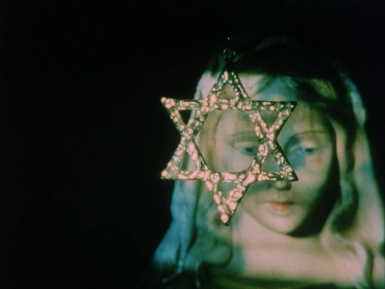 Subconscious Cruelty (2000) movie still: closeup — A dark, nondescript interior space features a close view of a religious statue. A gold Star of…