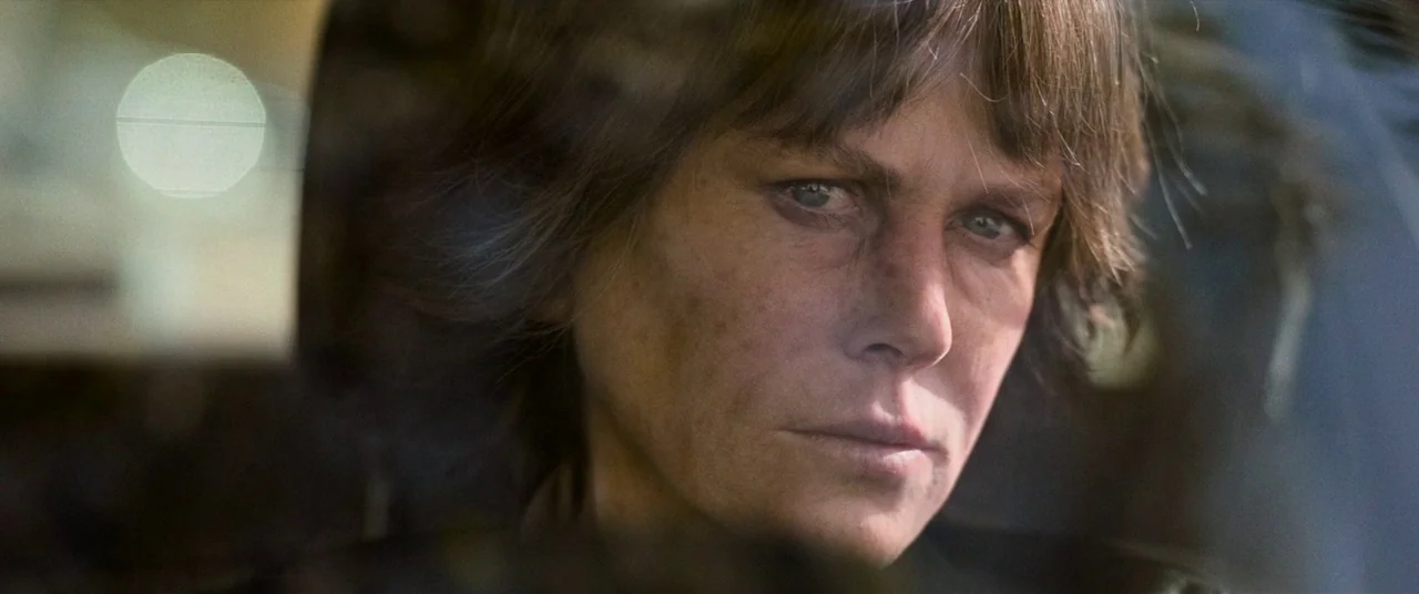 Destroyer (2018) movie still: closeup — A close-up of a woman sitting in the driver's seat of a car. Reflections appear on the window as she stares…