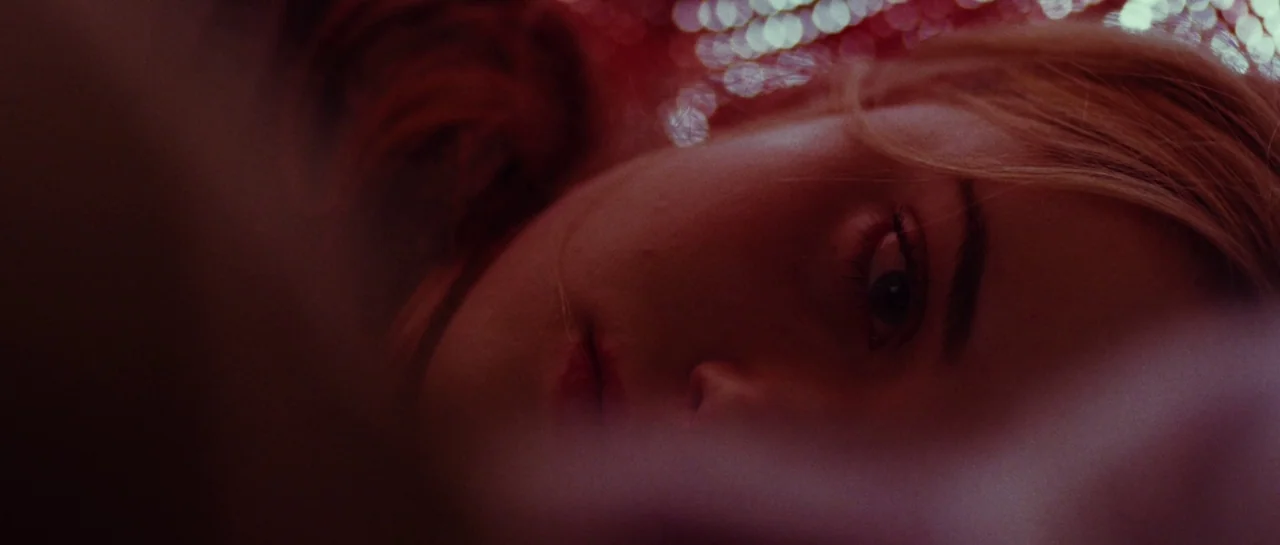 Starfish (2018) movie still: closeup — A woman's face is framed in a shallow depth of field against a dark background. Red lighting catches the…